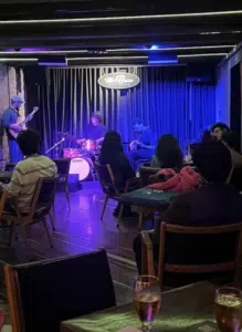 A band performs on stage in a dimly lit Bogotá bar as patrons seated at tables watch and listen.